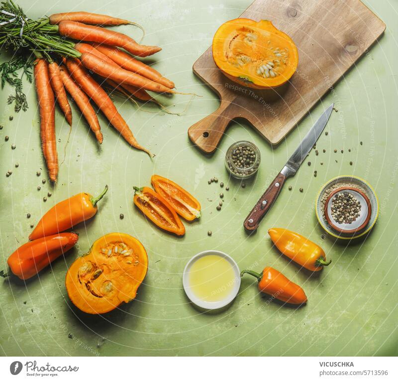 Orange color vegetables cooking preparation on green table with cutting board and kitchen utensils, top view. Healthy and clean food orange color