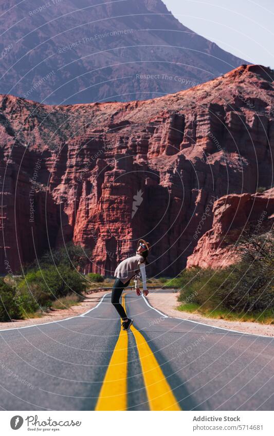 Individual playfully balancing on the road's yellow lines with the striking red formations of Los Castillos in the background individual balance Argentina