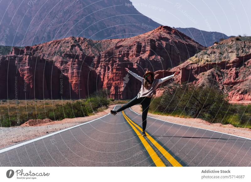 Joyful individual dancing on an open road amidst the stunning red cliffs of Los Castillos, with a clear sky above joyful dance Argentina desert scenic travel