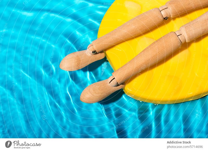 Body part of wooden mannequin figure sunbathing on a yellow pool float in clear blue swimming pool water Mannequin summer relaxation leisure sunny floating