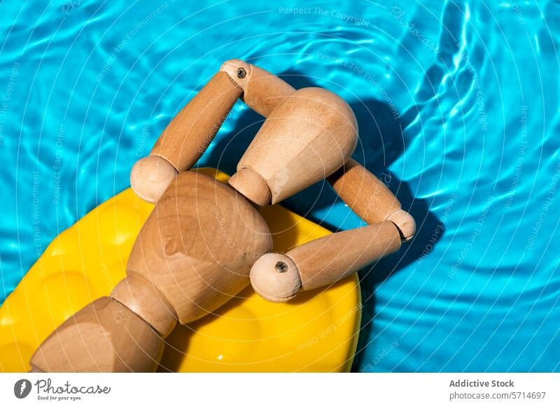 Wooden artist's mannequin relaxing on a yellow pool float in clear blue swimming pool water, simulating a summer leisure scene Mannequin relaxation wooden toy