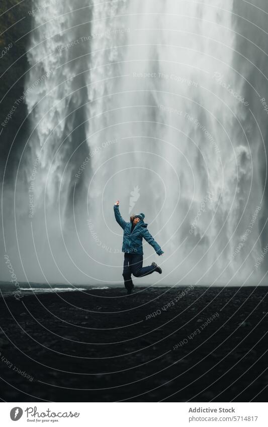 Woman jumping joyfully in front of a majestic Icelandic waterfall iceland woman female traveler exploration adventure nature powerful backdrop thrill black sand