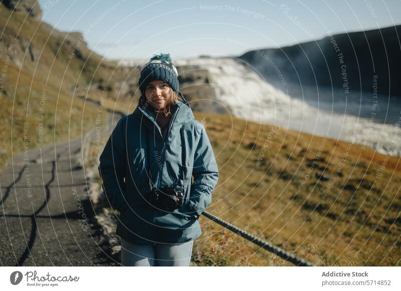 Woman tourist at Gullfoss Waterfall in sunny Iceland iceland woman female traveler gullfoss waterfall blue jacket knitted hat smile landscape nature outdoor