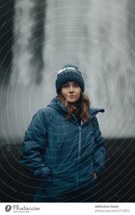 Young woman in blue jacket against misty waterfall backdrop iceland travel nature serene beanie female contemplative outdoors adventure exploration icelandic