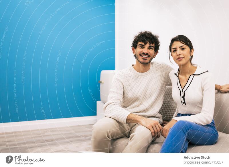 Casual couple relaxing together on a sofa at home comfort smile posing young casual cozy white couch blue wall interior man woman sitting room domestic life
