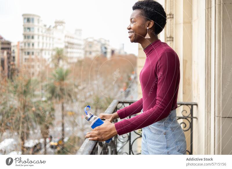 Smiling black woman with water bottle on urban balcony cityscape smiling reusable eco-friendly happy hydration environmental outdoors city life casual outfit