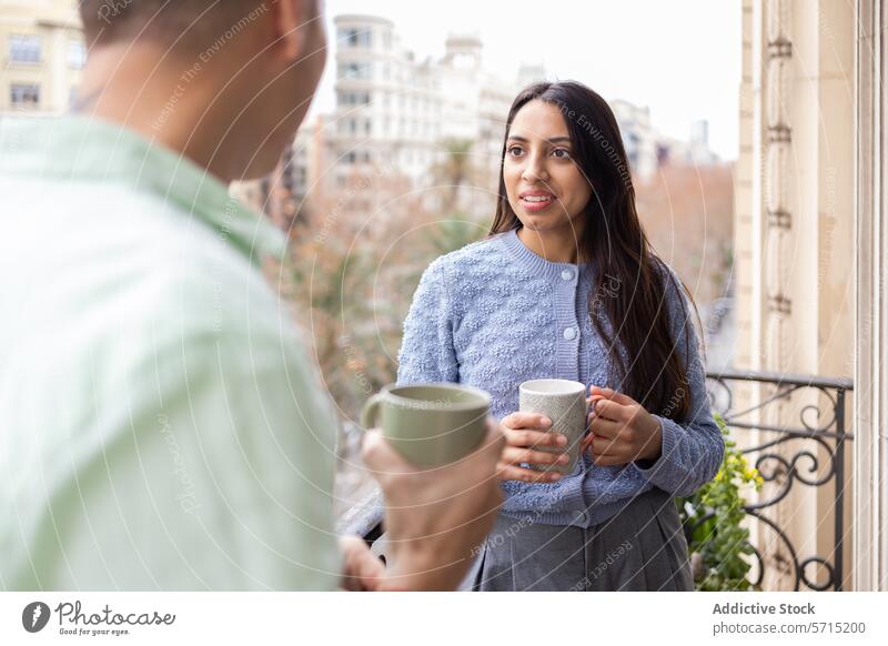 Couple enjoying coffee on a balcony with city view woman couple mug conversation smile urban building apartment leisure morning beverage warm knitwear sweater