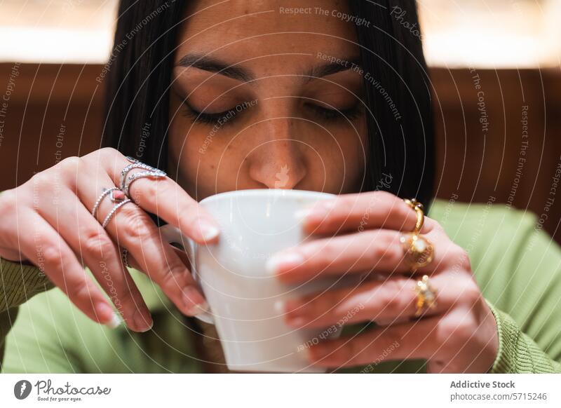 Young woman enjoying a hot beverage indoors coffee cup sip intimate cozy hot drink young adult dark hair rings jewelry fashion delicate relaxation coffee break