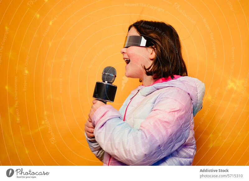 Joyful girl singing into a microphone, wearing futuristic glasses and a colorful jacket, on a yellow background joyful music performance entertainment child