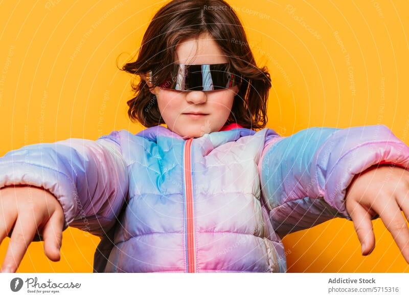Confident girl posing with futuristic glasses and extending her hands forward, wearing a colorful pastel jacket against an orange background pose child fashion