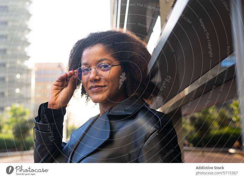 Confident woman adjusting her glasses, dressed in a trendy black coat, with modern architecture in the background Woman confident style fashion urban chic