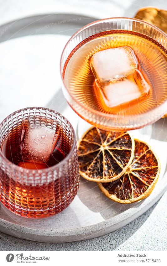 Vibrant alcoholic drinks served in textured glasses, accented with ice cubes and garnished with dehydrated orange slices on a sunny day vibrant beverage