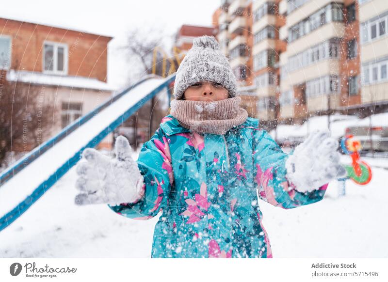 A child in a colorful jacket playing with snow in a playground during winter Child outdoor snowflake activity cold fun enjoyment playful knit hat scarf mittens