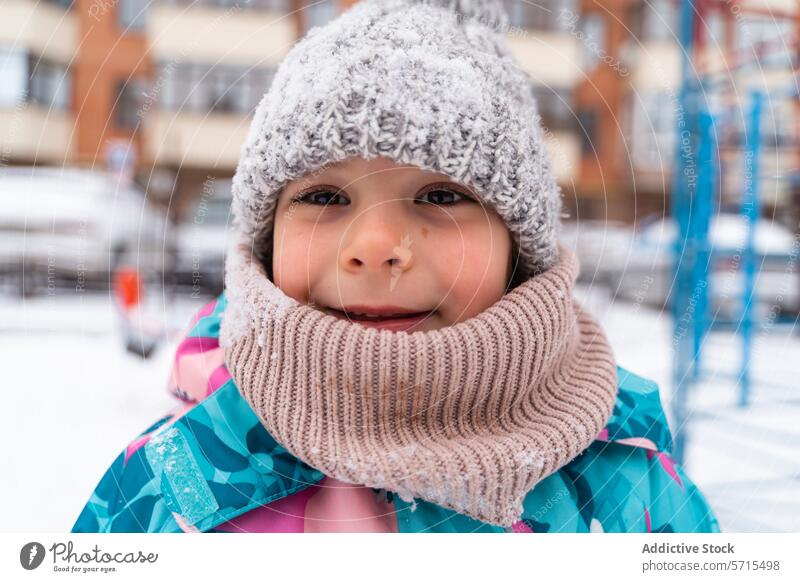 Smiling child in a knitted hat and scarf outdoors with a snowy playground in the background Child smile winter cheerful happiness cold weather joy youthful fun