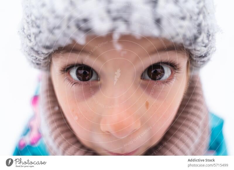 Close-up of a child's eyes looking up, wearing a woolen hat in a snowy setting Child gaze close-up winter outdoor curiosity innocence face warmth knitwear cold