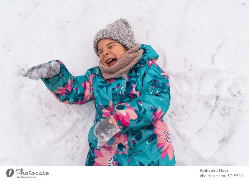 Child laughing joyfully while making a snow angel, dressed in a vibrant winter coat and hat outdoor cold playful scarf fun woolen activity chill happiness