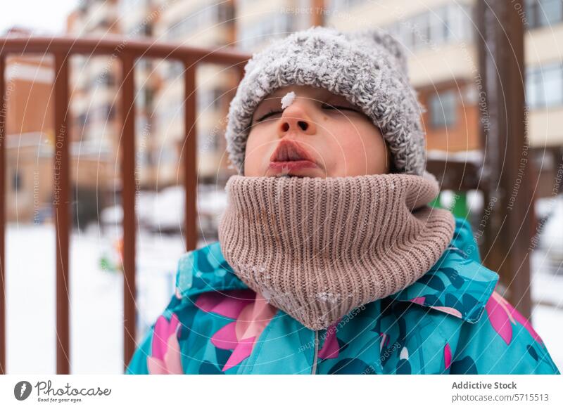 Child in a colorful jacket catching snowflakes with mouth open against a playground backdrop winter outdoor playful cold woolen hat scarf fun joy activity