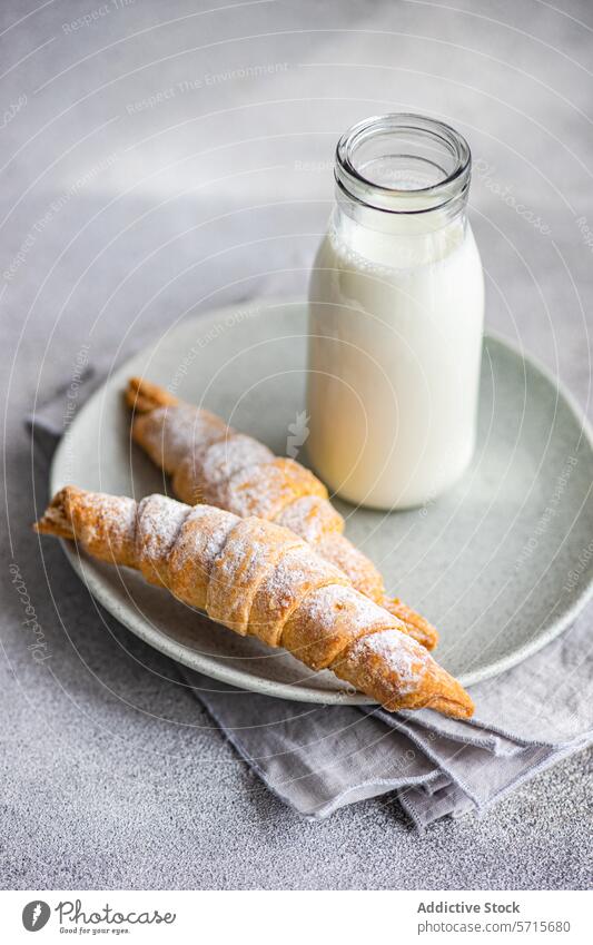 Two homemade jam-filled pastry cones with a dusting of powdered sugar, accompanied by a bottle of milk, on a ceramic plate over a grey napkin and countertop