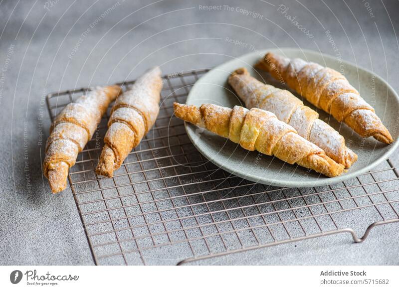 Freshly baked homemade pastry cones filled with sweet jam, dusted with powdered sugar, served on a ceramic plate with a cooling rack on a grey countertop Pastry