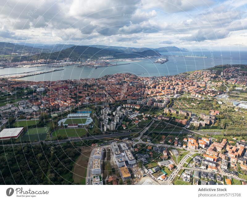 Aerial view of cityscape with sports fields and coastline aerial drone building sea ship mountain cloud sky urban area landscape green lush modern architecture
