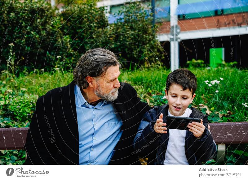 Grandfather and grandson enjoying technology on a park bench grandfather smartphone family bonding generation elderly child boy man interaction attention