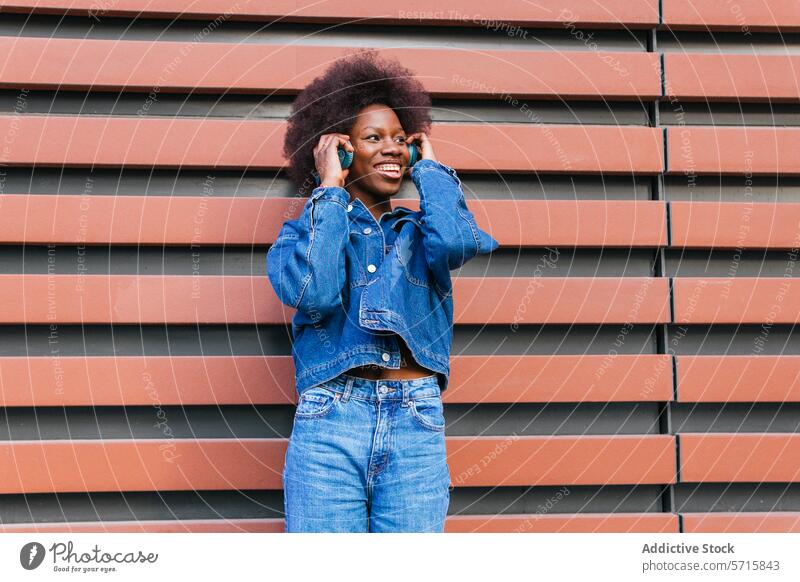 A radiant woman enjoys her favorite tunes, dressed head to toe in classic denim against a geometric terracotta backdrop music headphones fashion rhythmic vibes