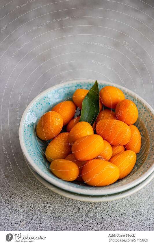 Top view of vibrant bowl of fresh kumquats with a green leaf, placed on a textured grey surface fruit citrus cloth ripe healthy snack vitamin juicy sweet tart