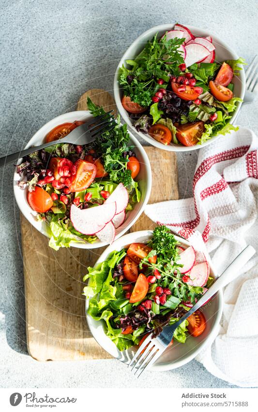 Top view of fresh vegetable salads with lettuce, arugula, radishes, cherry tomatoes, and pomegranate seeds on a wooden board with a kitchen towel Salad healthy