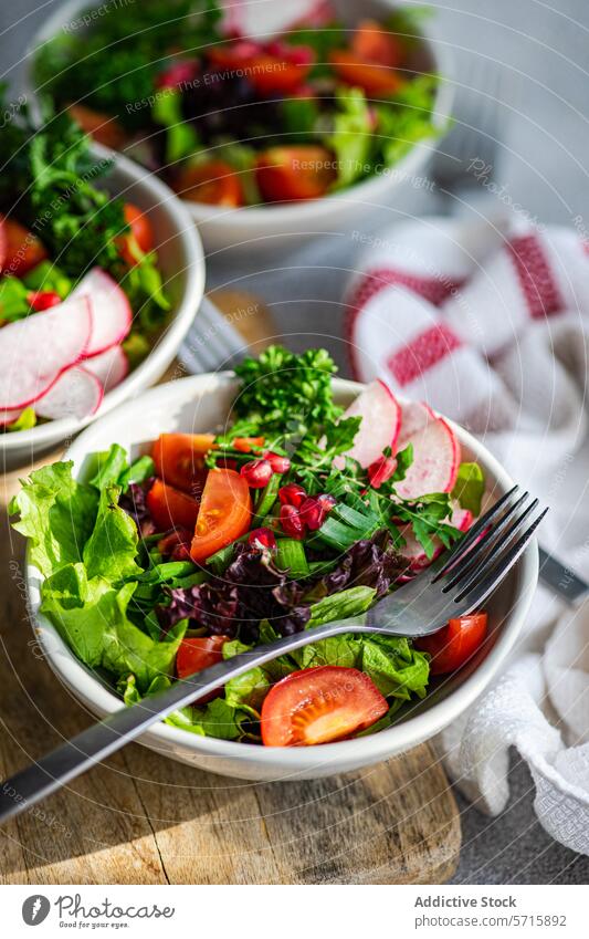 A close-up of a bowl of colorful vegetable salad with lettuce, arugula, radishes, cherry tomatoes, and pomegranate seeds on a wooden cutting board Salad healthy