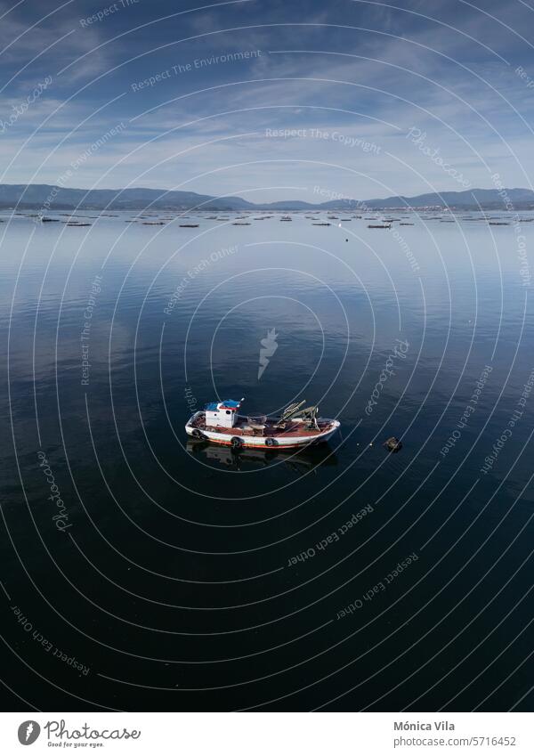 A small wooden fishing boat anchored in the Arousa estuary. Mussel farming polygon wooden boat Galicia Galician coast aerial view drone bateas bateas polygon