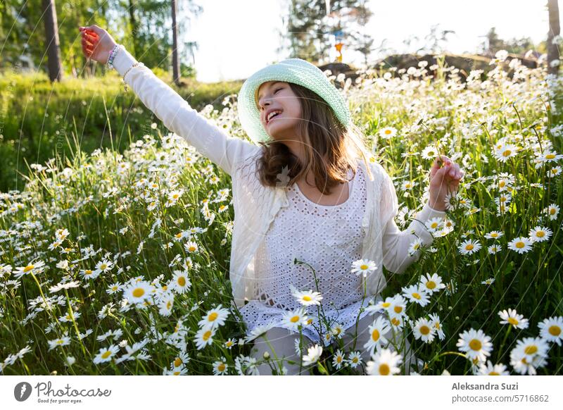 Girl sitting on a meadow covered with wild flowers. Background of field of daisy flowers in bloom. Sunny summer day, rays of light. Summer vacation concept