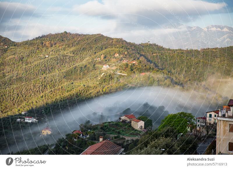 Panoramic top view of Alps mountains in fog and clouds, valley in sunrise. Medieval buildings of Perinaldo town, Liguria, Italy alpine alps amazing ancient