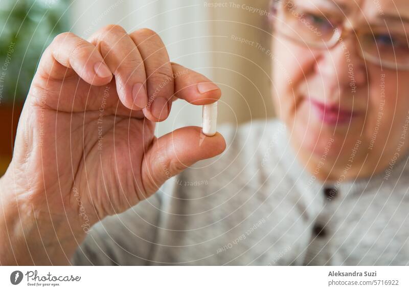Senior Woman Taking Medication, holding pill in hand, looking though glasses. Elderly Person with concerned face reading prescription on medicine bottle. adult