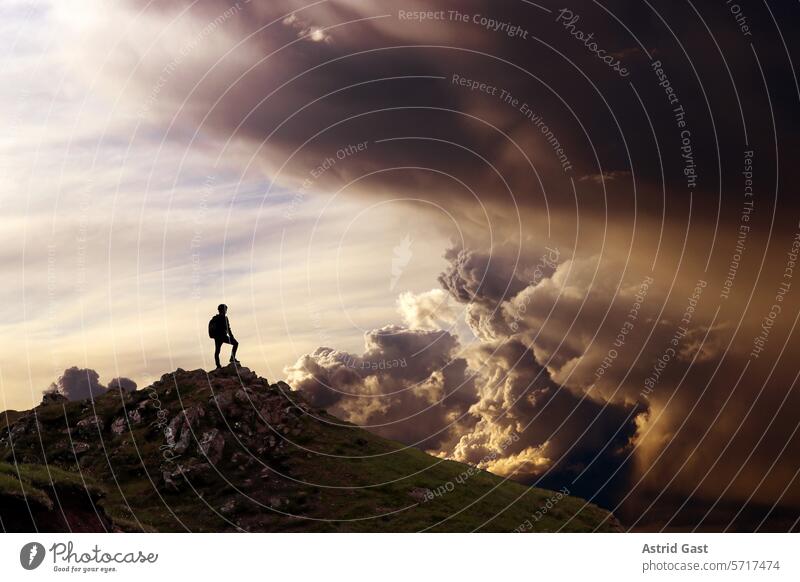 A man stands on a mountain and looks into a fantastic cloudscape Man Mountaineer Peak Sky Clouds Fantastic cloud formation Sunset Sunrise Thunder and lightning