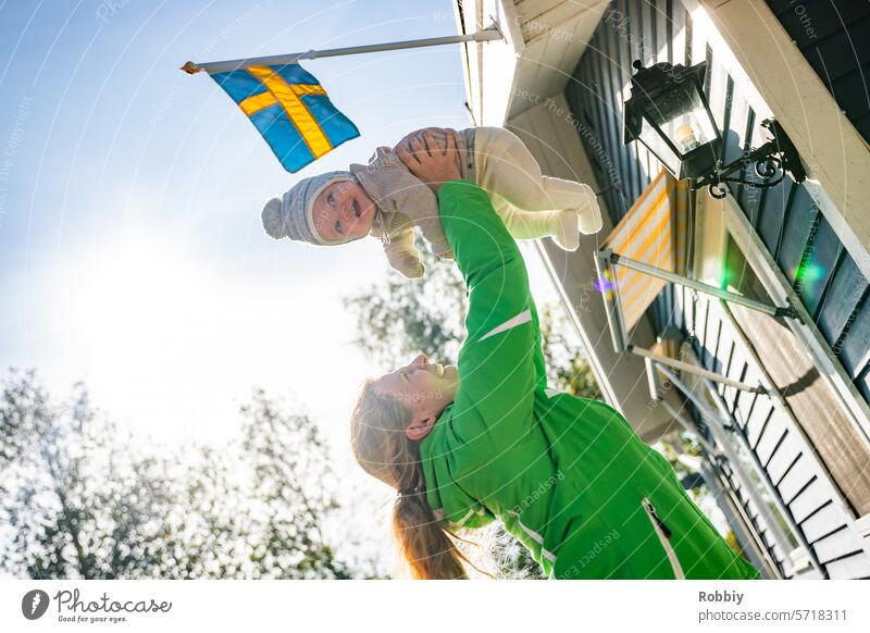 Mother lifts baby into the air in front of a Swedish cabin Parents mama Baby Child Toddler Infancy Swede maternity Joy Family Smiling Lifestyle Woman