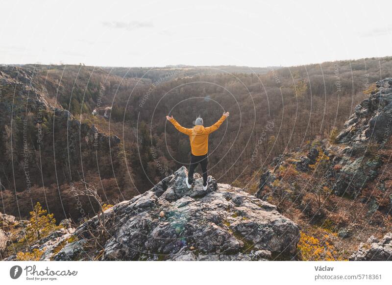 Traveller in a yellow jacket standing on the edge of a rock enjoying a moment of relaxation and a view of the Divoke sarky valley, Prague, Czech Republic. Achieving success