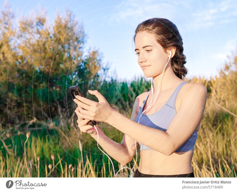 Woman in sportswear looking at her mobile phone in the park woman fitness exercise street sunset technology health athlete female city outdoor lifestyle young