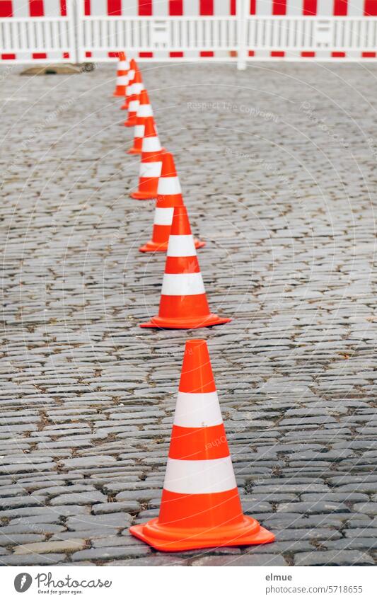 Traffic cones in a row and red and white barrier fence on a paved road guiding cone cordon Pylons paving Street Road safety Reddish white Transport