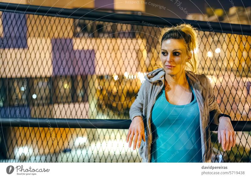Portrait of woman athlete wearing casual sportswear resting over banister at night in urban setting female runner portrait young metallic railing thoughtful