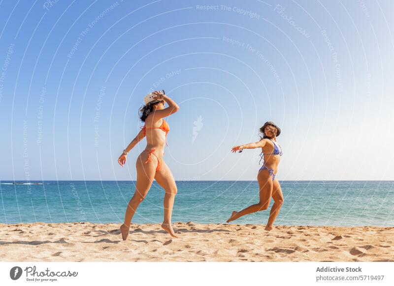 Two friends playfully dancing on the sand, sporting bright bikinis and hats, embodying the spirit of a carefree beach day dance ocean fun friendship joy summer