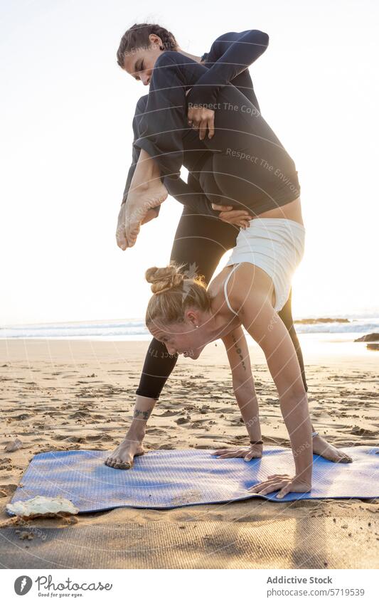 Yoga Duo Practising Poses On Beach At Sunset yoga beach sunset practice pose forward bend assistance fitness wellness health sand duo partnership balance
