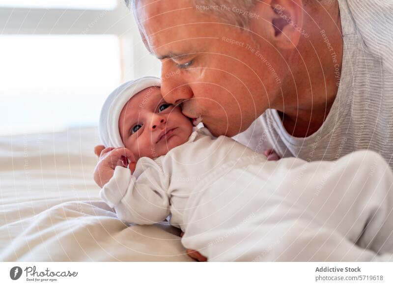 A father lovingly kisses his newborn's forehead while the baby looks on with wide eyes, creating a heartwarming family moment kissing embrace tender wide-eyed