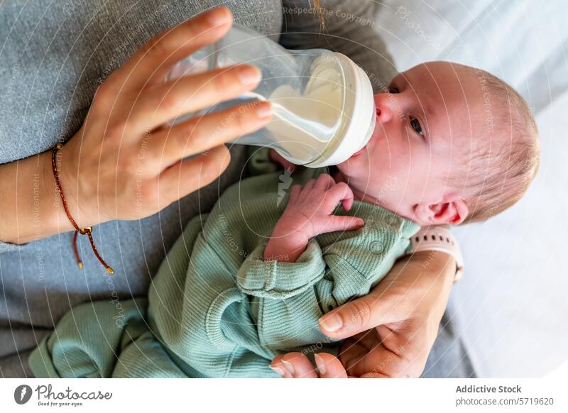 A newborn is comfortably cradled in anonymous mother's arms, being fed with a milk bottle, depicting a nurturing and caring moment feeding nurture care baby