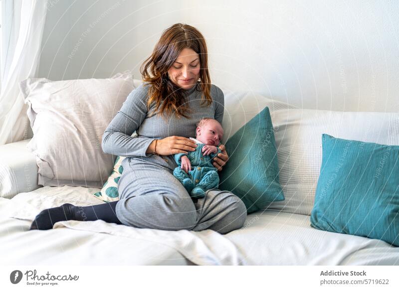 A serene mother sits on a sofa, cuddling her newborn baby close, surrounded by comfortable pillows in a bright room infant family bonding maternal love care