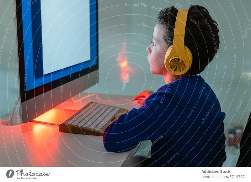 A child is intently using a computer, illuminated by the warm backlight of the monitor, with headphones on engaged technology keyboard concentration student