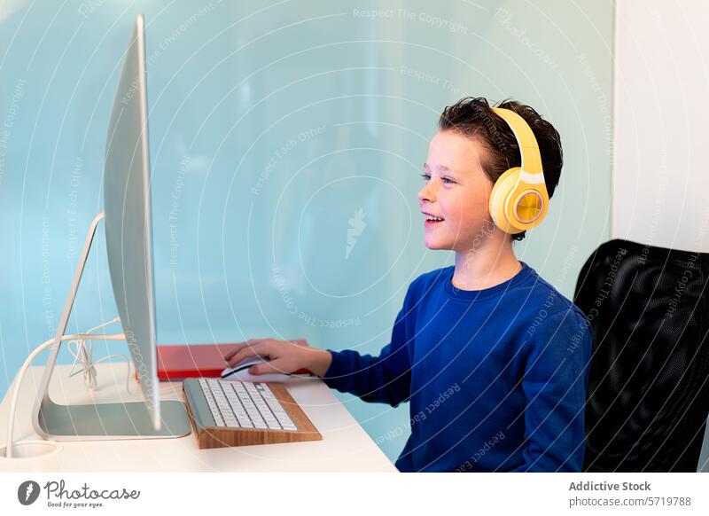 A cheerful child interacts with a computer, wearing bright yellow headphones, with a smile indicating enjoyment or success with the task at hand engagement