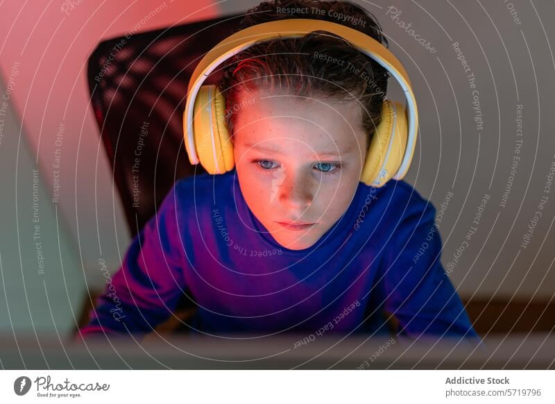 Intensely focused child with headphones using a computer, immersed in an online educational program or game learning technology screen e-learning intense