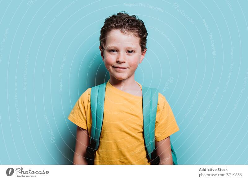 A happy young boy with a backpack smiles against a turquoise background, exuding confidence and excitement for school confident child student education ready
