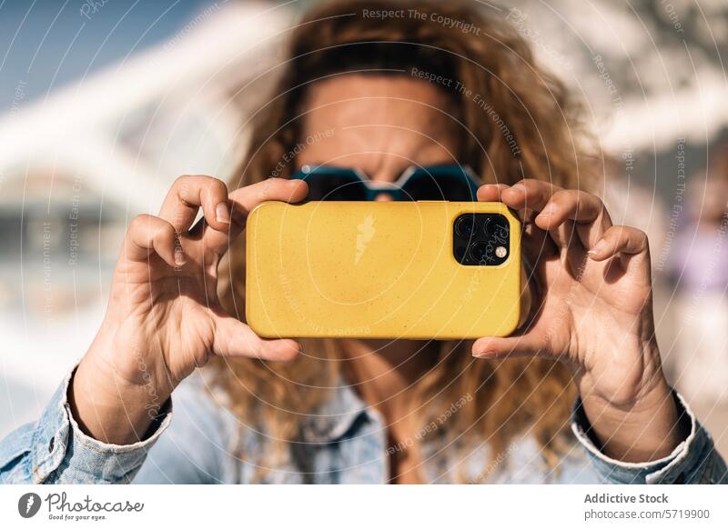 A person with distinctive hands, missing thumbs, captures a moment using a smartphone with a yellow case; the camera focus is on the adapted grip selfie