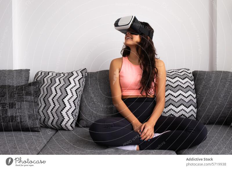Woman with VR headset seated on couch woman virtual reality vr cross-legged fitness yoga meditation athletic wear joyful living room latina young adult female